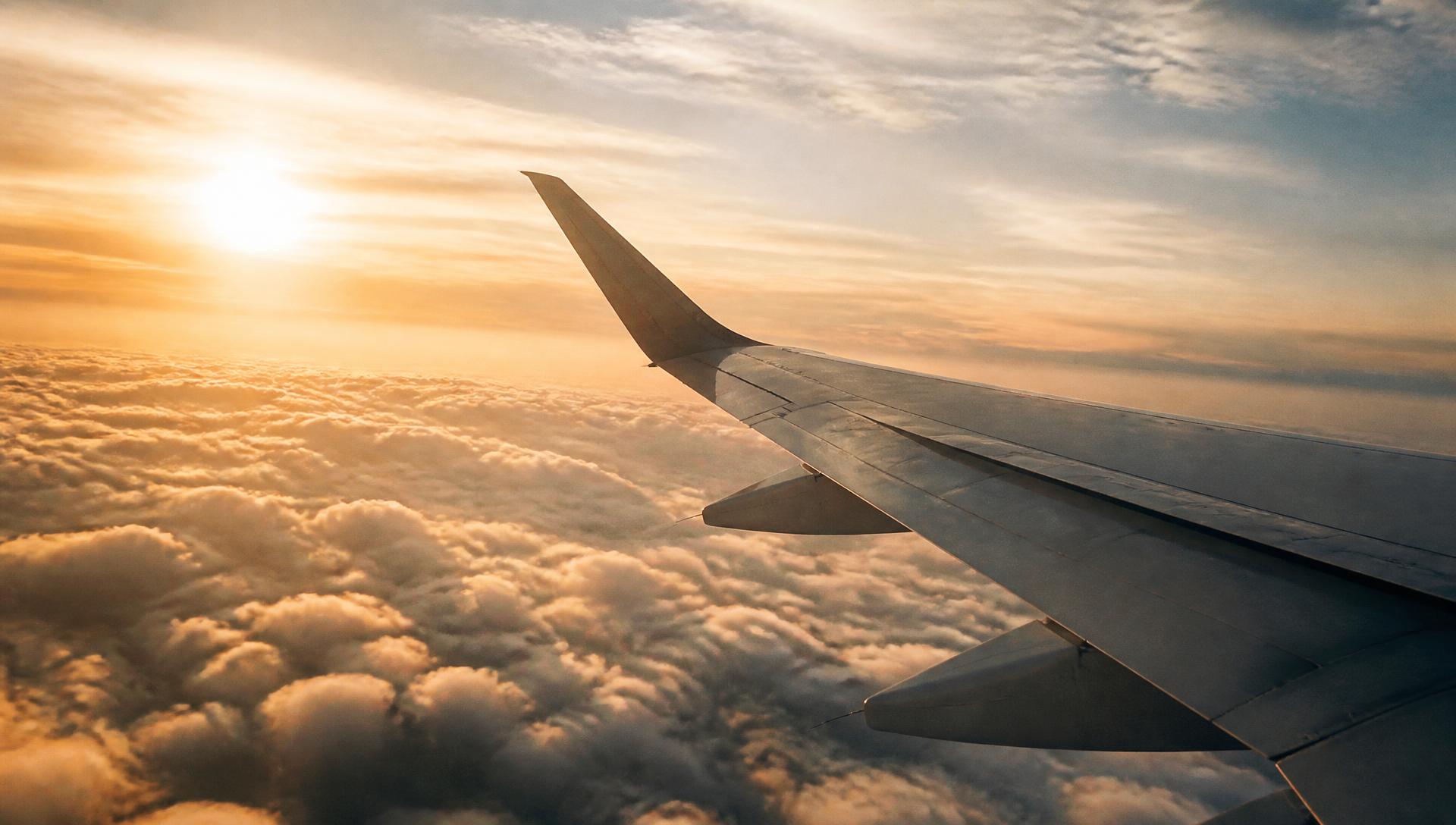 Aircraft wing above warm sunset clouds